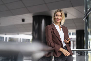 Portrait of smiling young businesswoman with mobile phone in the city - DIGF08685