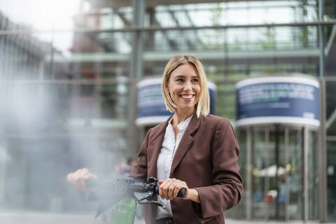 Happy young businesswoman with e-scooter in the city stock photo