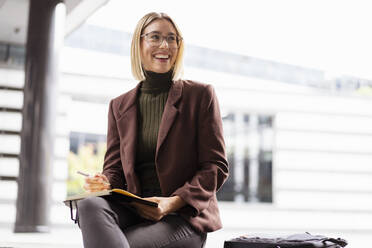 Smiling young businesswoman with notebook in the city - DIGF08708