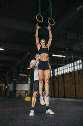 Young woman jumping to gymnastic rings, man helping her - MTBF00070