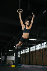 Junge Frau in schwarzer Sportkleidung beim Ring-Muscle-Up-Training mit Gymnastikringen - MTBF00075