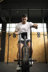 Athletic man doing air bike workout at gym - MTBF00078