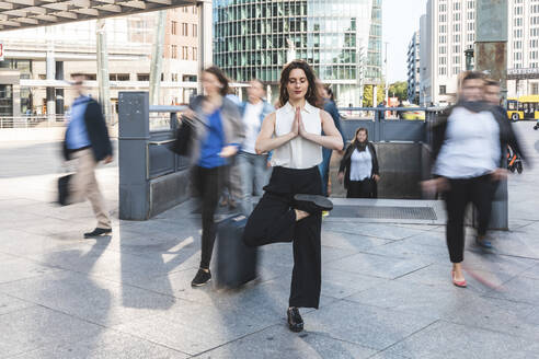 Young businesswoman practising yoga in the city at rush hour, Berlin, Germany - WPEF02181