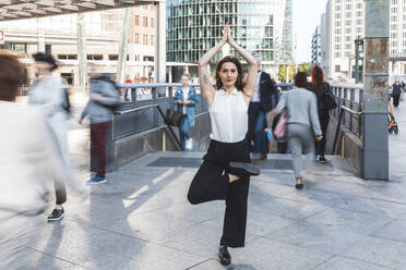 Junge Geschäftsfrau übt Yoga in der Stadt zur Hauptverkehrszeit, Berlin, Deutschland - WPEF02182