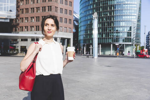 Junge Geschäftsfrau mit Kaffee zum Mitnehmen in der Stadt unterwegs, Berlin, Deutschland, lizenzfreies Stockfoto