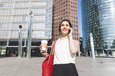 Smiling young businesswoman with takeaway coffee on the phone in the city, Berlin, Germany - WPEF02186