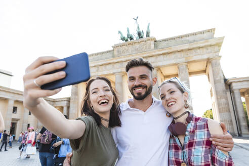 Porträt von drei glücklichen Freunden, die ein Selfie mit ihrem Handy vor dem Brandenburger Tor machen, Berlin, Deutschland - WPEF02214