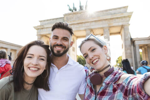 Porträt von drei glücklichen Freunden, die ein Selfie mit ihrem Handy vor dem Brandenburger Tor machen, Berlin, Deutschland, lizenzfreies Stockfoto