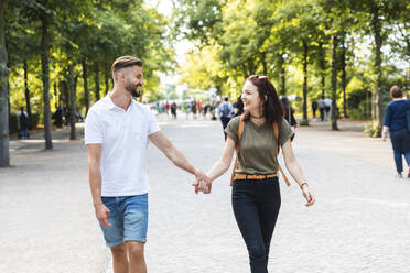 Glückliches junges Paar, das Hand in Hand in einem Park spazieren geht - WPEF02220