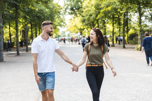 Glückliches junges Paar, das Hand in Hand in einem Park spazieren geht - WPEF02220