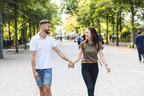 Happy young couple walking hand in hand in a park - WPEF02220