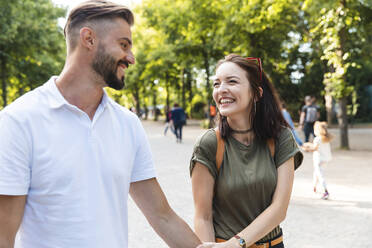 Porträt einer glücklichen jungen Frau, die Hand in Hand mit ihrem Freund in einem Park spazieren geht - WPEF02221