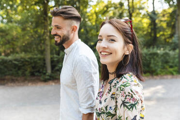Porträt eines glücklichen jungen Paares, das in einem Park spazieren geht - WPEF02226