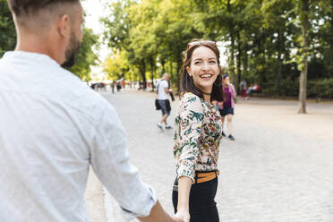 Porträt einer glücklichen jungen Frau, die Hand in Hand mit ihrem Freund in einem Park spazieren geht - WPEF02227