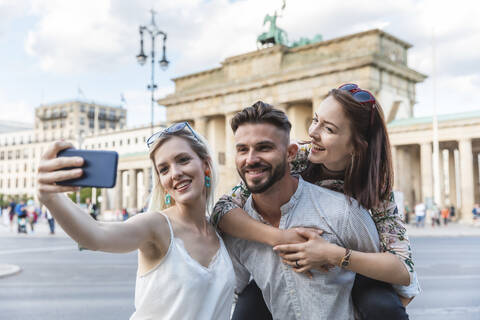 Porträt von drei Freunden, die ein Selfie mit dem Handy vor dem Brandenburger Tor machen, Berlin, Deutschland, lizenzfreies Stockfoto