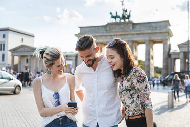 Drei Freunde schauen auf ihr Handy vor dem Brandenburger Tor, Berlin, Deutschland - WPEF02239