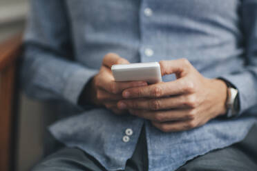 Midsection of man using smart phone while sitting on chair - CAVF66677