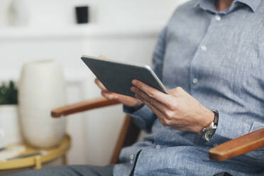 Midsection of businessman using tablet computer while sitting on chair in office - CAVF66678