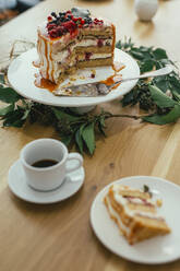 High angle view of cake on cake stand by cup and leaves at table - CAVF66687