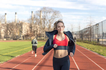 Female athlete running on sports track against sky - CAVF66694