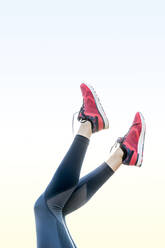 Low section of female athlete with feet up against clear sky - CAVF66696