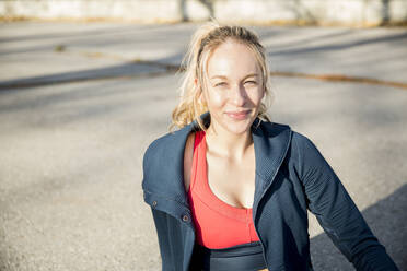 Portrait of smiling female athlete relaxing on footpath - CAVF66699