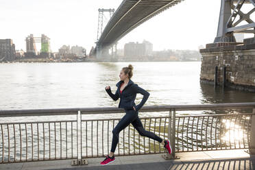 Seitenansicht eines selbstbewussten Sportlers, der auf der Promenade am East River läuft - CAVF66703