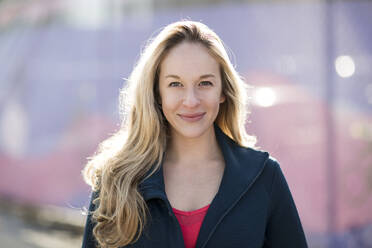 Close-up portrait of confident athlete standing by fence during sunny day - CAVF66709