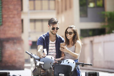 Junges Paar benutzt ein Smartphone, während es mit Fahrrädern steht - CAVF66770
