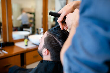 Hairdresser combing customer's hair in barber shop - CUF52898