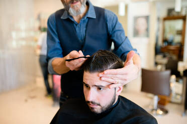 Friseurin stylt die Haare eines Kunden im Friseursalon - CUF52900