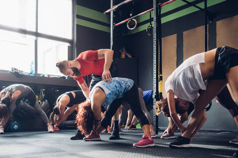 Frauen trainieren im Fitnessstudio mit einem männlichen Trainer und berühren ihre Zehen, lizenzfreies Stockfoto
