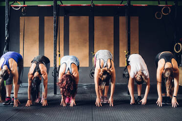 Row of women training in gym, bending forward touching floor - CUF52910