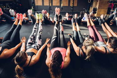 Große Gruppe von Frauen, die in einem Fitnessstudio trainieren, auf dem Boden sitzend und mit angehobenen Beinen - CUF52924