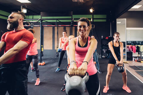 Frauen trainieren im Fitnessstudio mit männlichem Trainer, heben Kettlebells, lizenzfreies Stockfoto