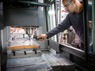 Arbeiter einer Messerfabrik sprüht Flüssigkeit auf Maschinen in einer Werkstatt - CUF52945