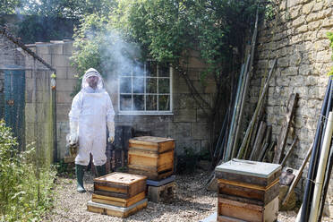 Männlicher Imker mit Bienenräuchermaschine in einem ummauerten Garten, Porträt - CUF52969