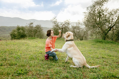 Mädchen kauert, um mit einem Labradorhund in einer malerischen Feldlandschaft zu spielen, Citta della Pieve, Umbrien, Italien, lizenzfreies Stockfoto