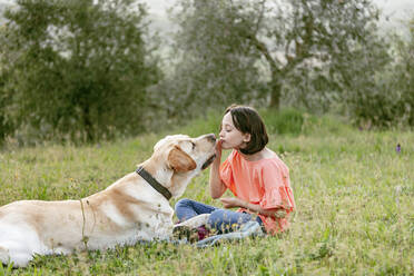 Mädchen sitzt mit Labradorhund in einer Feldlandschaft, Citta della Pieve, Umbrien, Italien - CUF52978