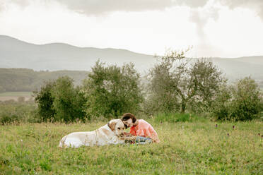 Mädchen sitzt und streichelt Labradorhund in malerischer Feldlandschaft, Citta della Pieve, Umbrien, Italien - CUF52979