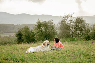 Mädchen sitzt und streichelt Labradorhund in malerischer Feldlandschaft, Citta della Pieve, Umbrien, Italien - CUF52980