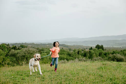 Mädchen läuft mit Labradorhund in malerischer Feldlandschaft, Citta della Pieve, Umbrien, Italien - CUF52984