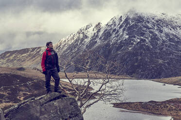 Männlicher Wanderer mit Blick auf einen See und eine schneebedeckte Berglandschaft, Llanberis, Gwynedd, Wales - CUF53007