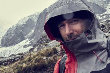 Männlicher Wanderer mit aufgesetzter Kapuze in schneebedeckter Berglandschaft, Nahaufnahme, Llanberis, Gwynedd, Wales - CUF53009