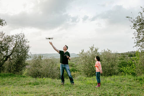 Mädchen beobachtet Vater fliegende Drohne in malerischer Feldlandschaft, Citta della Pieve, Umbrien, Italien - CUF53010
