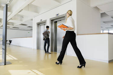 Businesswoman and businessman in office corridor - CUF53104