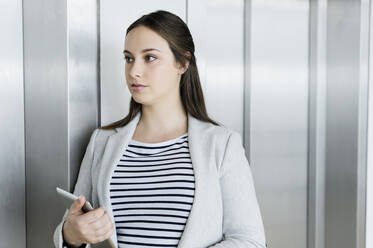 Businesswoman with digital tablet leaning against elevator door - CUF53129