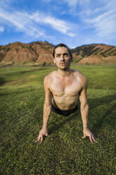 Ernster Mann ohne Hemd übt Yoga auf einer Wiese vor den Bergen im Bridger-Teton National Forest - CAVF66783