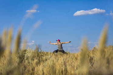 Mann mit ausgestreckten Armen übt Yoga auf einem Feld gegen den Himmel im Bridger-Teton National Forest - CAVF66787