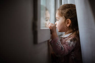 Seitenansicht eines jungen Mädchens, das aus dem Fenster auf den Regen schaut - CAVF66839